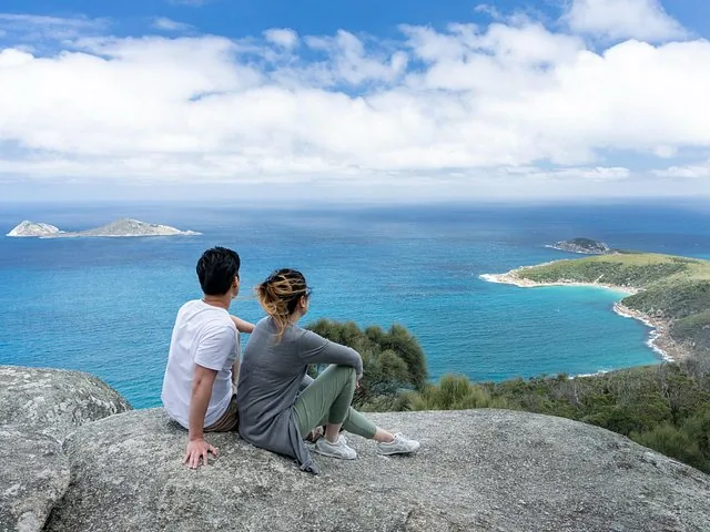 Pareja sentada en un saliente rocoso contemplando el océano azul y las islas.