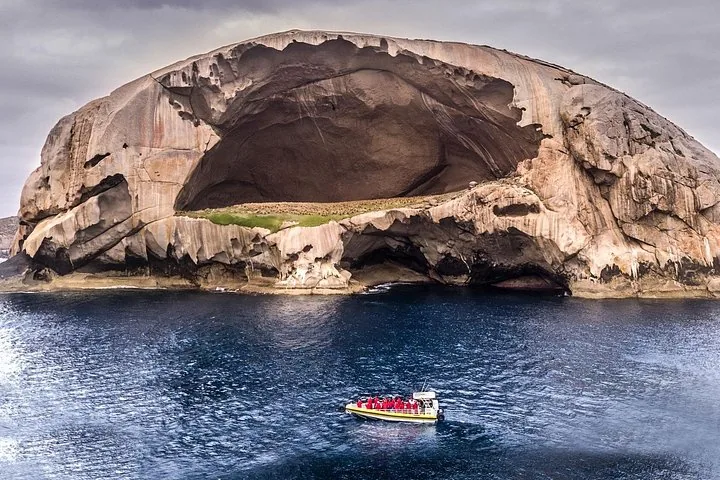 Barco turístico amarillo navegando cerca de Skull Rock, una enorme isla de granito con una cueva.