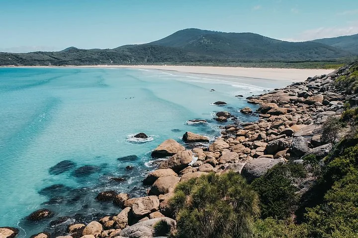 Acque turchesi e limpide che si infrangono su una spiaggia sabbiosa con grandi rocce.