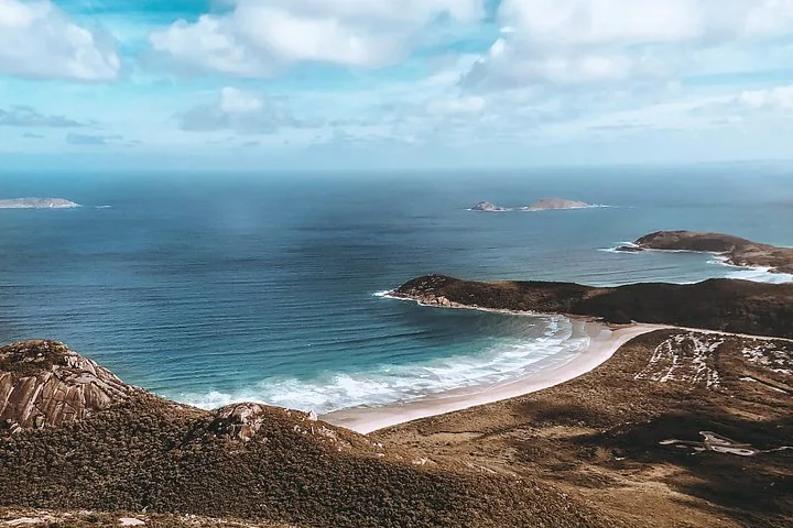 Veduta aerea di una lunga spiaggia sabbiosa curva e di una costa frastagliata che incontra l'oceano.